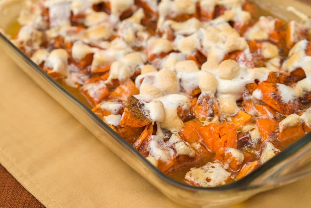A glass casserole dish with Candied Yams and Sweet Potatoes on top of a gold placemat. 