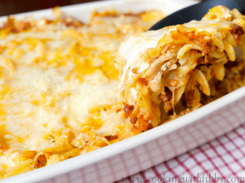A black spoonful of pasta mixed with spaghetti sauce and cheese in a baking dish.
