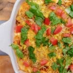 A horizontal picture of a Taco Casserole Recipe topped with cilantro, diced tomatoes, and shredded cheese.