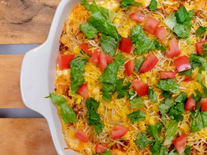 A horizontal picture of a Taco Casserole Recipe topped with cilantro, diced tomatoes, and shredded cheese.