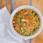 A square picture of Chinese Fried Rice in a cream colored bowl with a white napkin laid on the side.