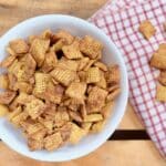 Peanut Butter Chex Mix in a small bowl on a wood pallet with a red and white napkin.
