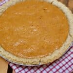 A picture of a whole Sweet Potato Pie Recipe on a gingham napkin and a wood pallet.