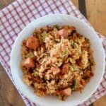 A featured image of a dirty rice recipe in a bowl on top of a red and white gingham cloth with a wooden slab.