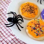 Orange and Purple Halloween Sugar Cookies with a black spider on a white plate.